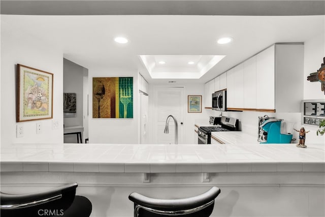 kitchen featuring a raised ceiling, appliances with stainless steel finishes, tile counters, and white cabinets