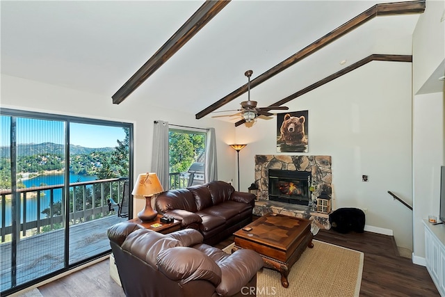 living room with a water and mountain view, ceiling fan, vaulted ceiling with beams, dark wood-type flooring, and a stone fireplace