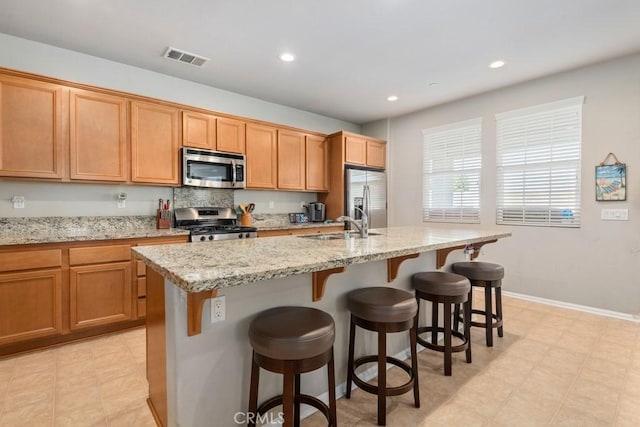 kitchen with stainless steel appliances, a center island with sink, and light stone countertops