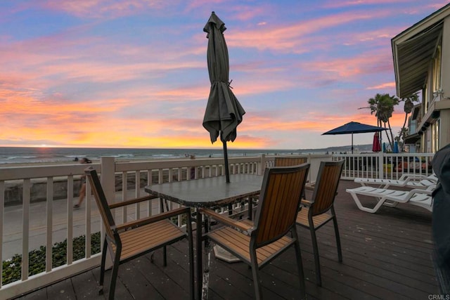 deck at dusk featuring a water view and a beach view