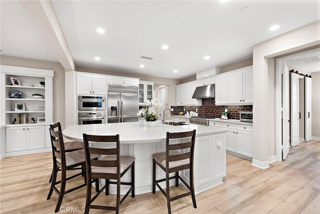 kitchen with white cabinetry, stainless steel appliances, wall chimney exhaust hood, a large island with sink, and sink