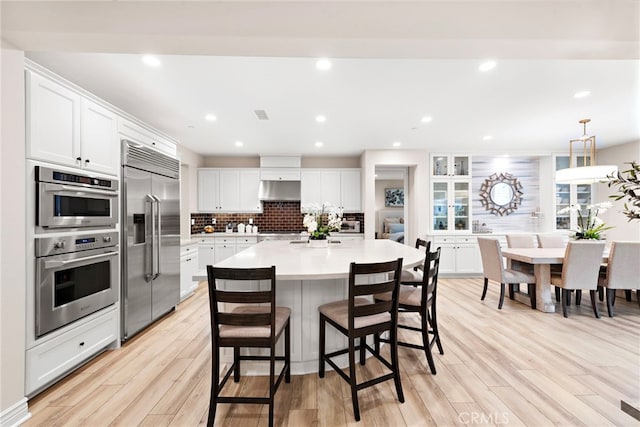 kitchen with white cabinetry, stainless steel appliances, decorative backsplash, decorative light fixtures, and a center island