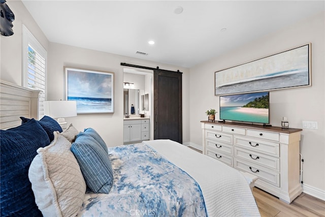 bedroom with ensuite bath, a barn door, and light wood-type flooring