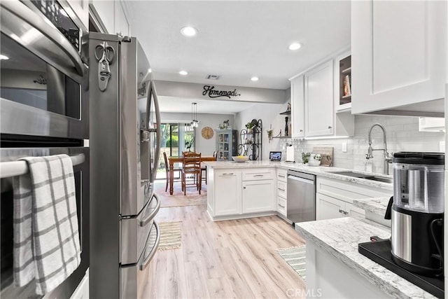 kitchen with kitchen peninsula, stainless steel appliances, sink, light hardwood / wood-style flooring, and white cabinetry