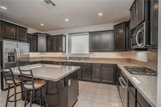 kitchen featuring appliances with stainless steel finishes, a kitchen breakfast bar, light stone counters, sink, and a kitchen island