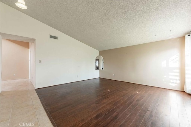 unfurnished room with hardwood / wood-style flooring, lofted ceiling, and a textured ceiling