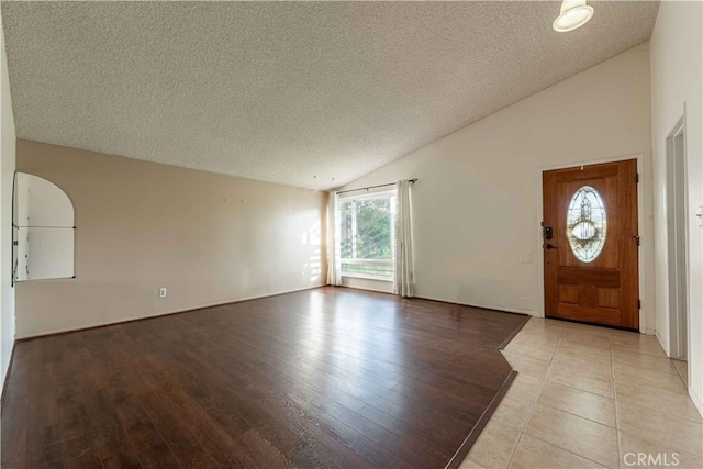 foyer with vaulted ceiling, light hardwood / wood-style floors, and a textured ceiling