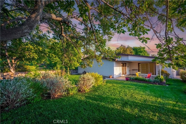 back house at dusk featuring a lawn