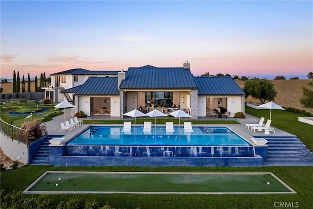 back of property at dusk featuring a patio, metal roof, a chimney, a lawn, and a standing seam roof