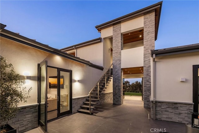 view of exterior entry featuring stone siding, a patio, and stucco siding