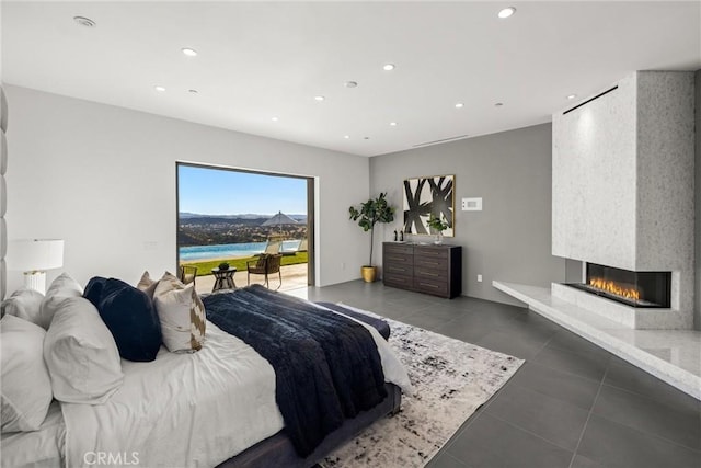 bedroom with a multi sided fireplace, a water view, and dark tile patterned flooring