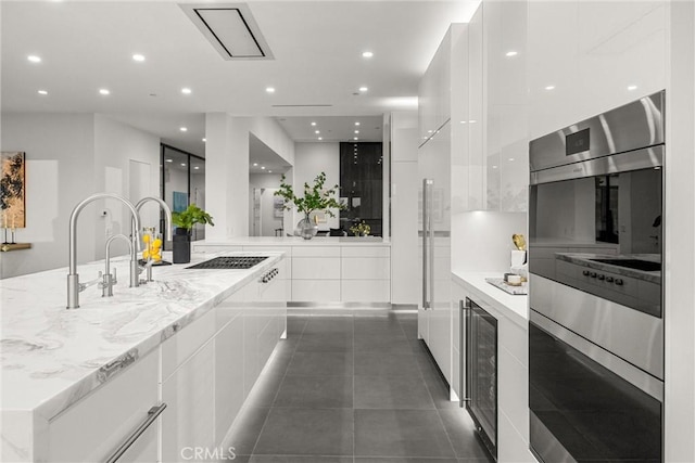 kitchen featuring dark tile patterned floors, double oven, light stone counters, white cabinetry, and beverage cooler