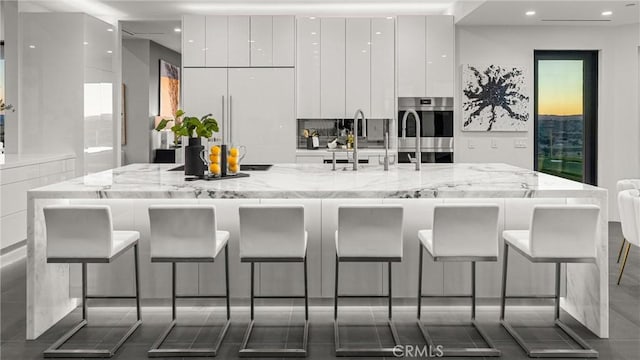 kitchen with a kitchen breakfast bar, stainless steel double oven, white cabinetry, and light stone counters