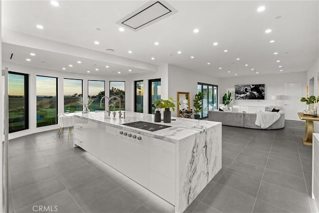 kitchen with light tile patterned floors, light stone counters, a spacious island, black electric cooktop, and white cabinets