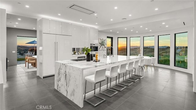 kitchen with light stone countertops, a kitchen breakfast bar, paneled fridge, a spacious island, and white cabinetry