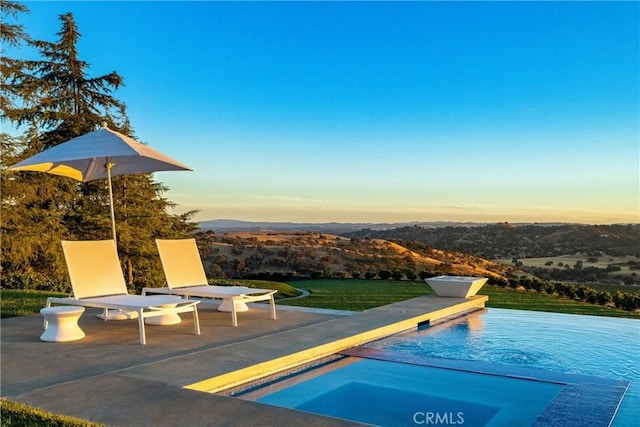 pool at dusk featuring an in ground hot tub, a patio, and a lawn