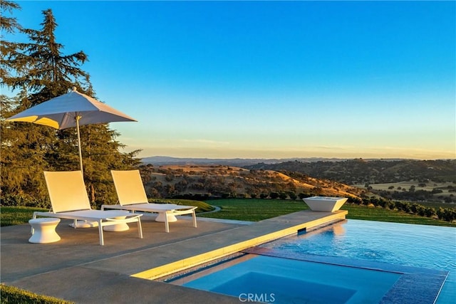 pool at dusk with a patio area and an outdoor pool
