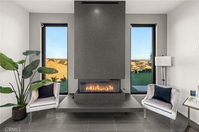 sitting room with a warm lit fireplace, tile patterned flooring, and plenty of natural light