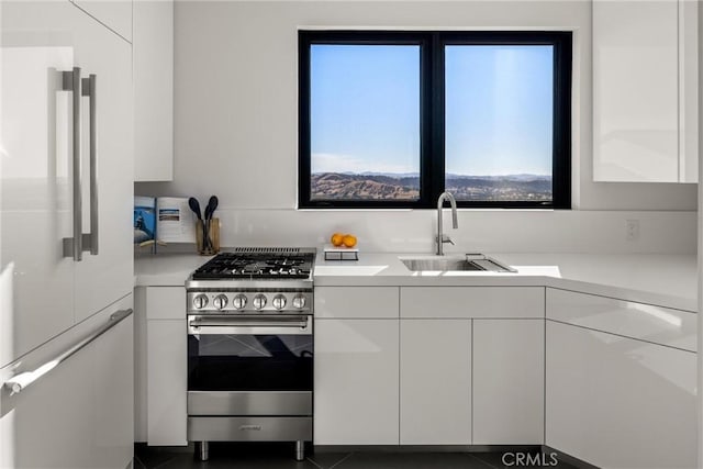 kitchen with a sink, stainless steel range with gas stovetop, refrigerator, light countertops, and white cabinets