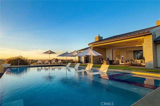 pool at dusk with a patio area, a pool with connected hot tub, and outdoor lounge area