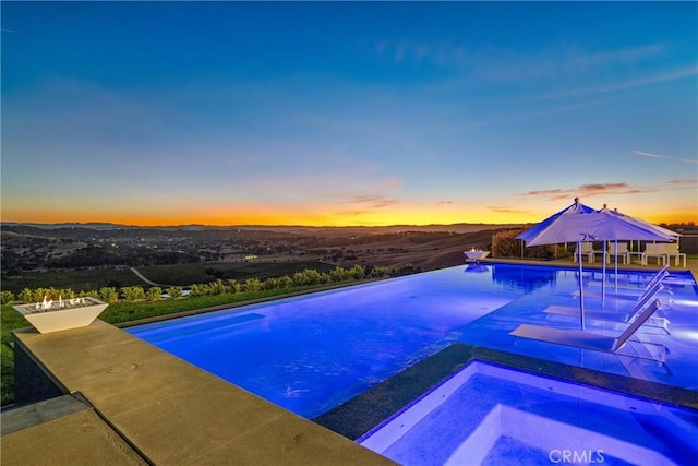 pool at dusk with an in ground hot tub