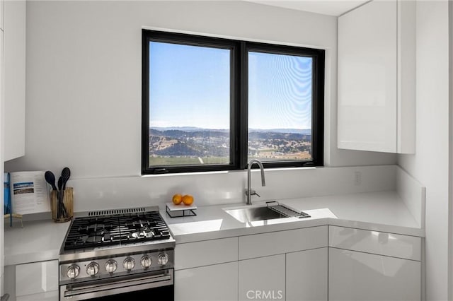 kitchen with stainless steel range with gas cooktop, light countertops, white cabinets, and a sink