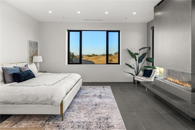 bedroom with recessed lighting, multiple windows, dark tile patterned flooring, and a glass covered fireplace