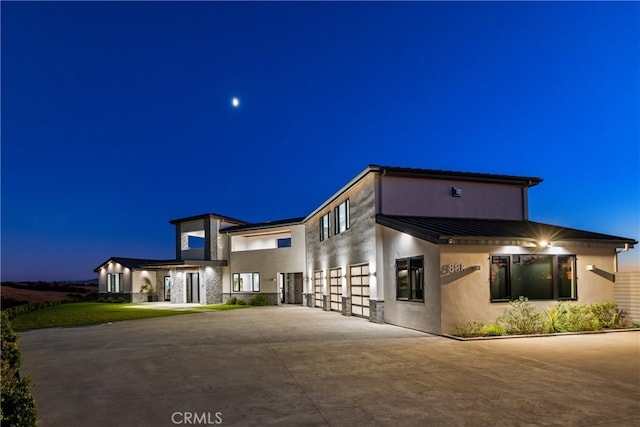 view of front facade featuring stone siding, stucco siding, metal roof, curved driveway, and a standing seam roof