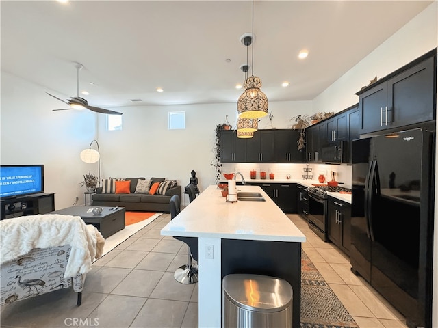 kitchen featuring black appliances, sink, an island with sink, hanging light fixtures, and light tile patterned floors