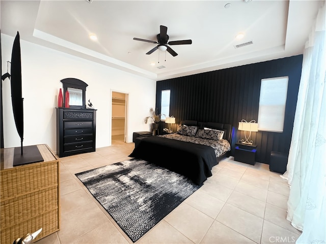 tiled bedroom featuring ceiling fan, a tray ceiling, multiple windows, and a walk in closet