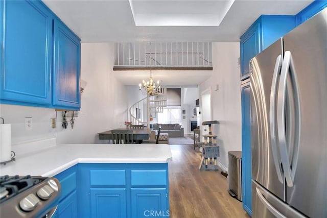 kitchen with blue cabinets, appliances with stainless steel finishes, a peninsula, a notable chandelier, and a tray ceiling