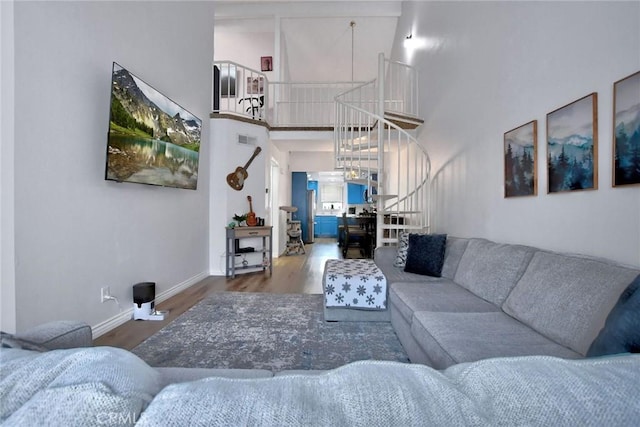 living room featuring baseboards, wood finished floors, a towering ceiling, visible vents, and stairway
