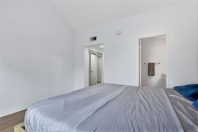 bedroom with ensuite bathroom, hardwood / wood-style flooring, and vaulted ceiling