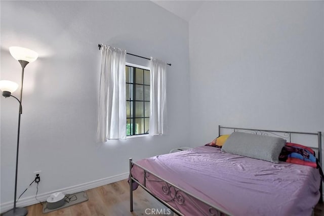 bedroom featuring baseboards, wood finished floors, and lofted ceiling
