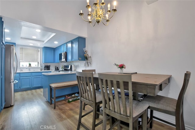 dining space featuring an inviting chandelier, hardwood / wood-style flooring, sink, and a raised ceiling