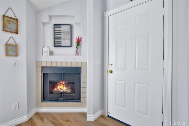 foyer featuring a warm lit fireplace, baseboards, and wood finished floors