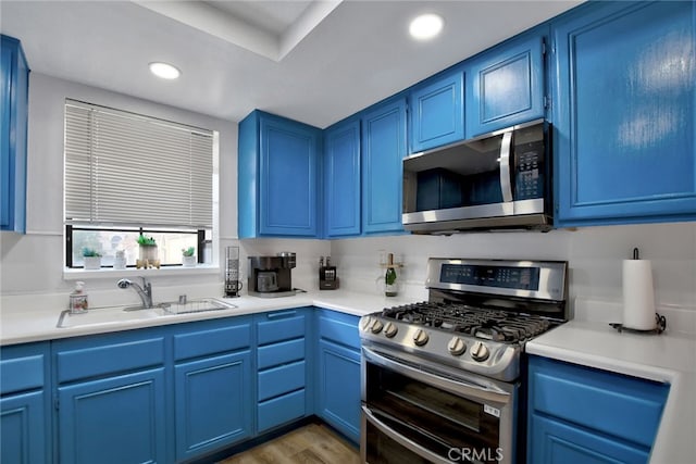 kitchen with appliances with stainless steel finishes, blue cabinetry, sink, and light wood-type flooring