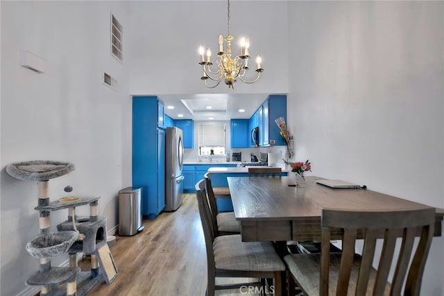 dining area with a high ceiling, light hardwood / wood-style flooring, sink, a raised ceiling, and a chandelier