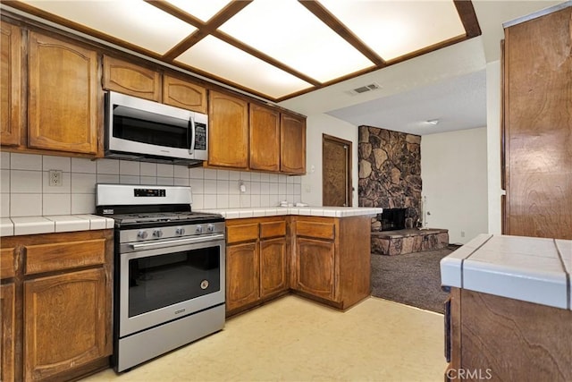 kitchen featuring kitchen peninsula, decorative backsplash, tile countertops, and appliances with stainless steel finishes