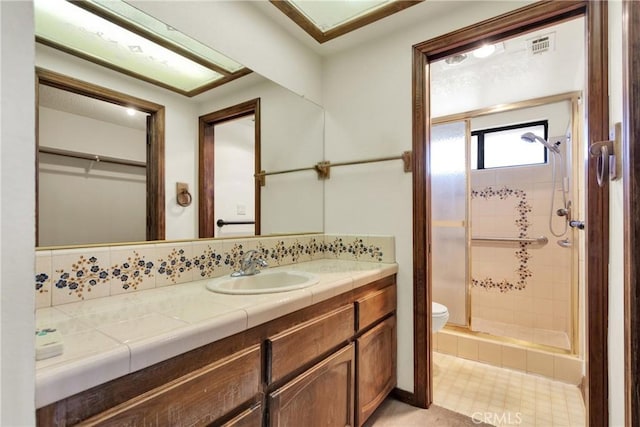 bathroom with backsplash, toilet, vanity, and tiled shower