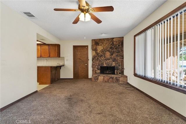 unfurnished living room with a textured ceiling, ceiling fan, carpet floors, and a fireplace