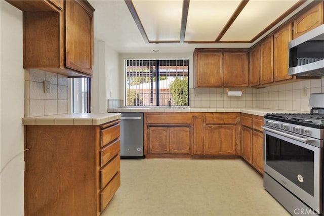 kitchen with appliances with stainless steel finishes, backsplash, tile countertops, and sink