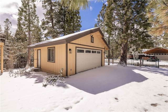 snow covered garage with a garage and fence