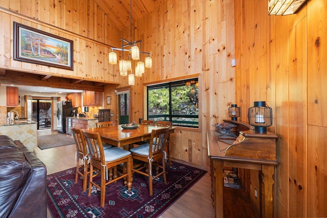 dining space with hardwood / wood-style flooring, sink, wooden walls, and high vaulted ceiling