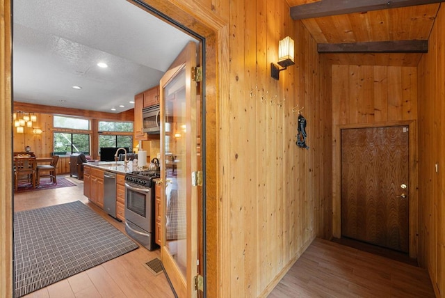 kitchen featuring stainless steel appliances, lofted ceiling with beams, light wood-type flooring, and wood walls