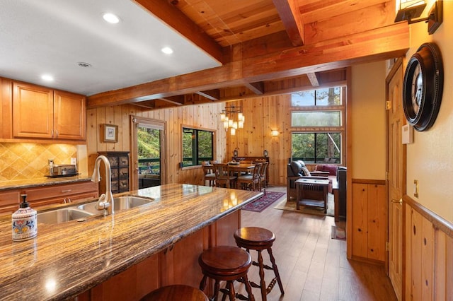 kitchen featuring sink, dark stone countertops, a kitchen breakfast bar, dark hardwood / wood-style floors, and beamed ceiling