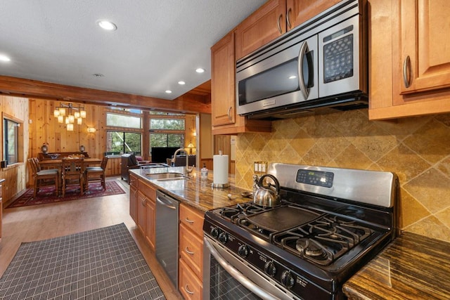 kitchen with sink, dark stone countertops, stainless steel appliances, dark hardwood / wood-style floors, and a notable chandelier