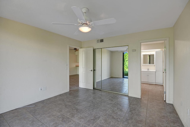 unfurnished bedroom with tile patterned floors, a closet, sink, ensuite bathroom, and ceiling fan