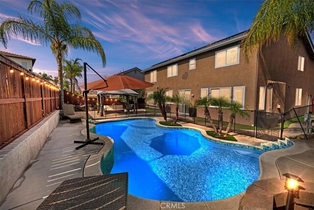 pool at dusk with a patio and a gazebo