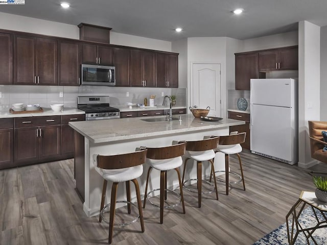 kitchen with sink, appliances with stainless steel finishes, hardwood / wood-style flooring, and an island with sink